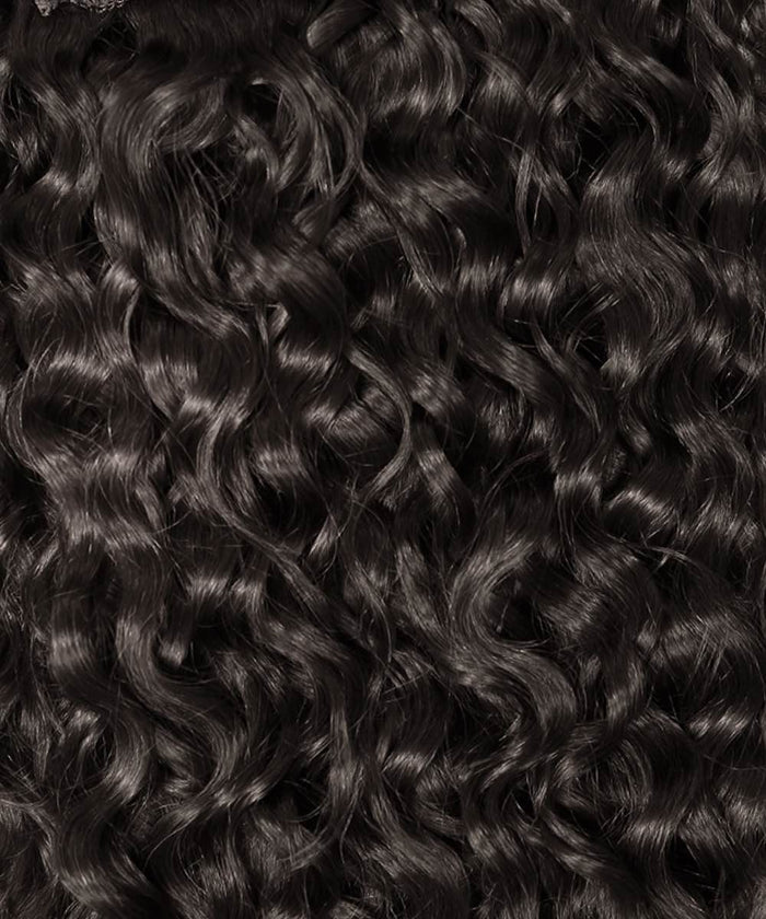 Close-up of tightly coiled, wavy-curly hair in Natural Black , shiny and healthy, ideal for blending with curly clip-ins.#color_natural-black-(1B)