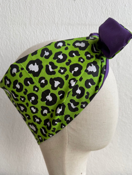 Green leopard print headscarf with purple bow on a mannequin head against a white background