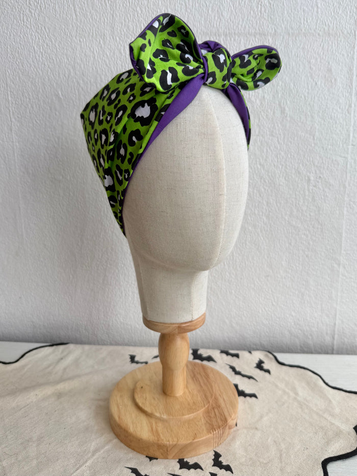 Green leopard print headscarf with purple accents on a mannequin head against a white background