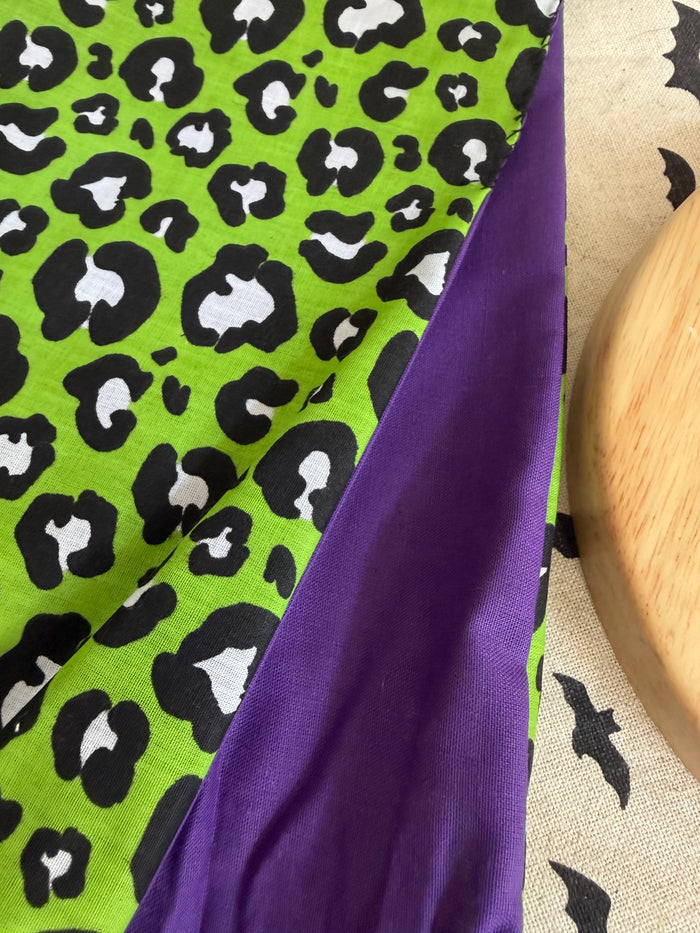 Fabric with green leopard print and purple border on a textured surface.