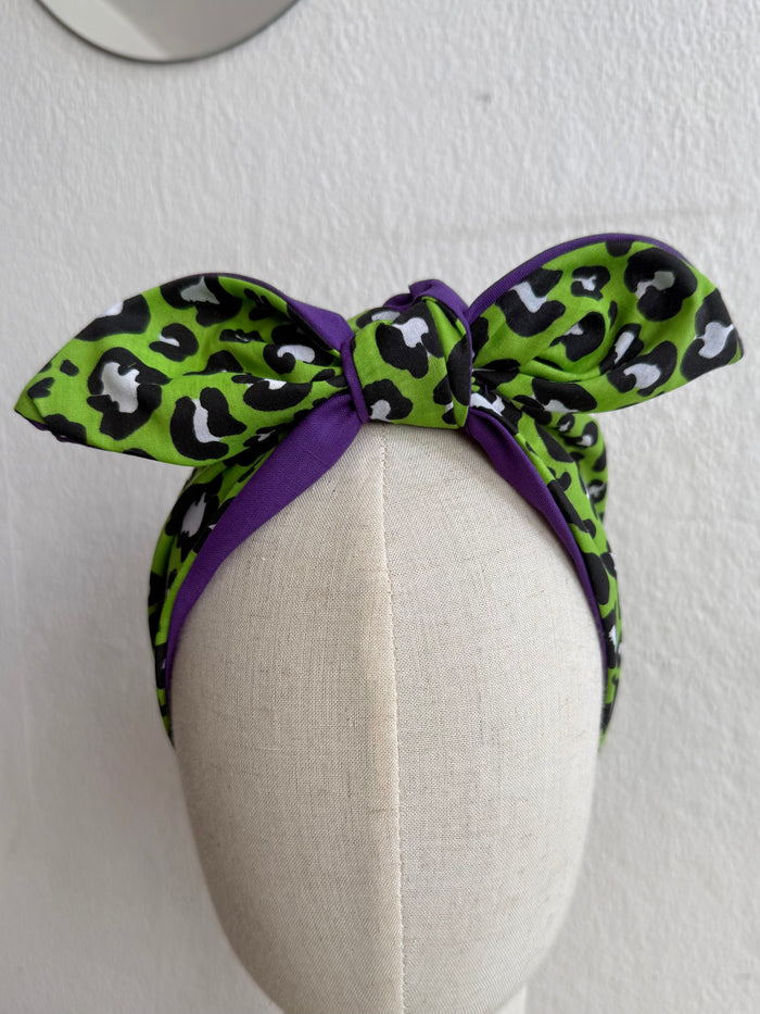 Green leopard print headband with purple bow on a mannequin head against a white background
