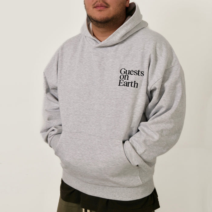 Guests on Earth Hoodie in heather grey, worn relaxed fit with minimalist chest logo and front pocket