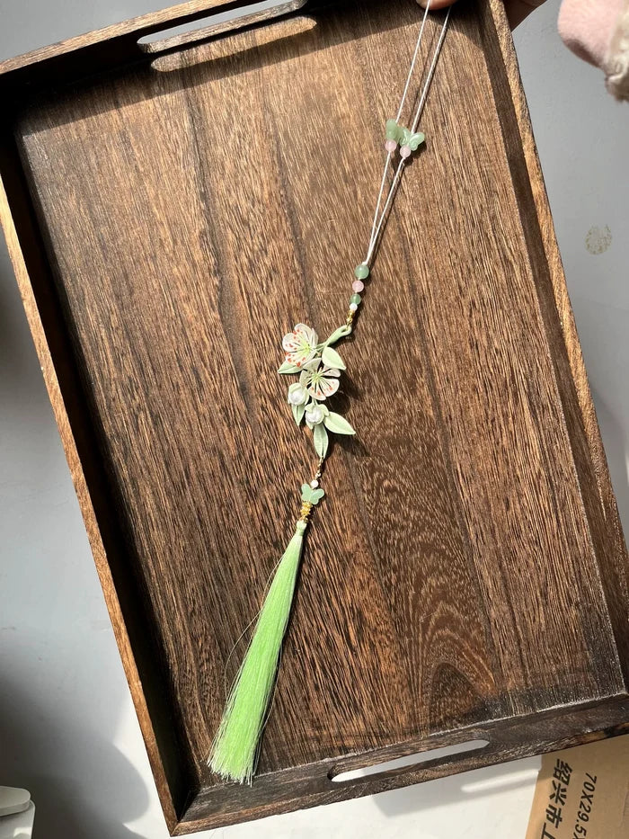 Handmade Chanhua pear blossom jinbu with a green tassel on a wooden tray