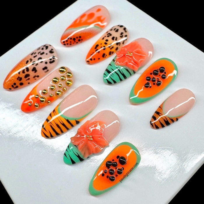 A set of 10 glossy press-on nails displayed on a white square card against a black background. The nails feature various designs including leopard print, tiger stripes, watermelon slices, gold studs, and coral flower accents.