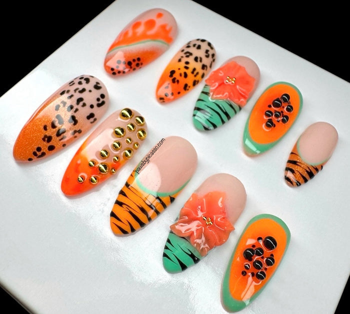 A set of artificial press-on nails displayed on a white square card against a black background. The nails feature various designs including leopard print, orange and green tropical patterns, tiger stripes, gold studs, and floral details.