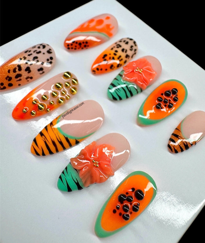 Ten almond-shaped press-on nails with vibrant tropical and animal-inspired designs, including orange and black stripes, leopard print, green and orange patterns, and a 3D orange flower accent, displayed on a light gray background.