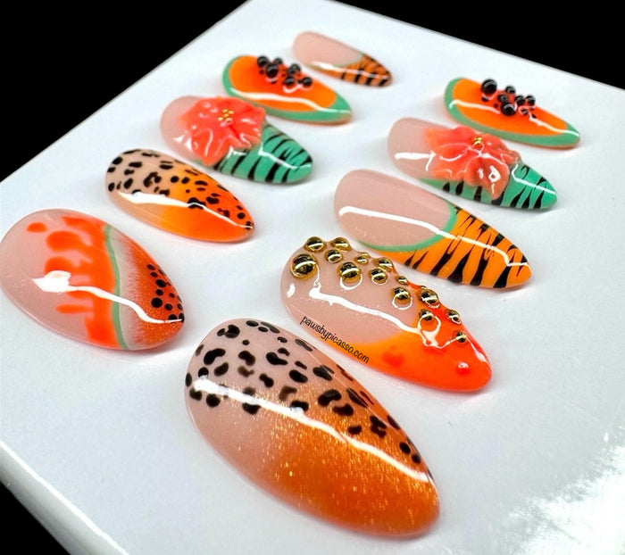 Ten almond-shaped press-on nails with vibrant tropical and animal-inspired designs, including orange and black stripes, leopard print, green and orange patterns, and a 3D orange flower accent, displayed on a light gray background.