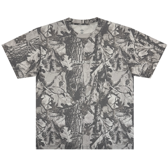 The Oaklandish Classic Logo Tee by Oaklandish is a heavyweight, short-sleeve oversized t-shirt in grey forest camo with tree bark, oak leaves, and pinecones. "OAKLANDISH" is printed in white across the chest. Shirt shown flat on a white background.