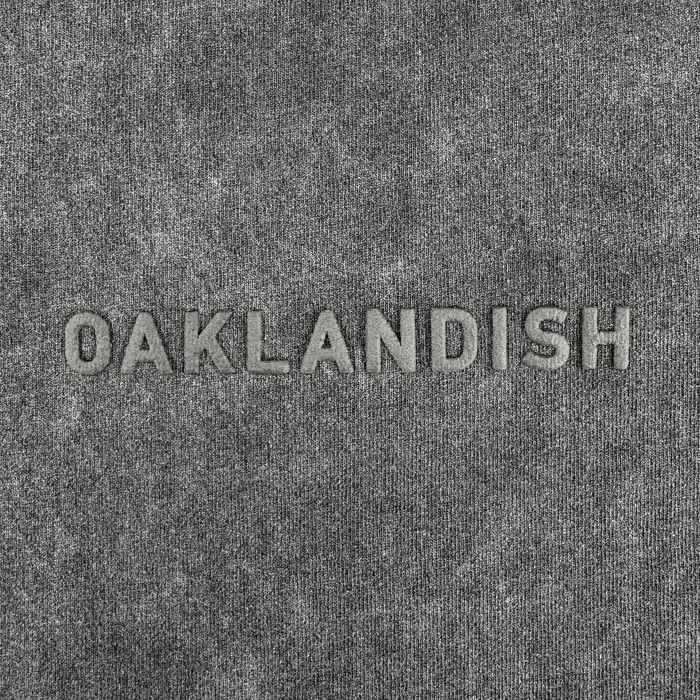 The Oaklandish Classic Logo Tee by Oaklandish features heavyweight gray textured cotton and bold raised “OAKLANDISH” embroidery in a lighter gray centered across the faded black, oversized shirt for subtle contrast.