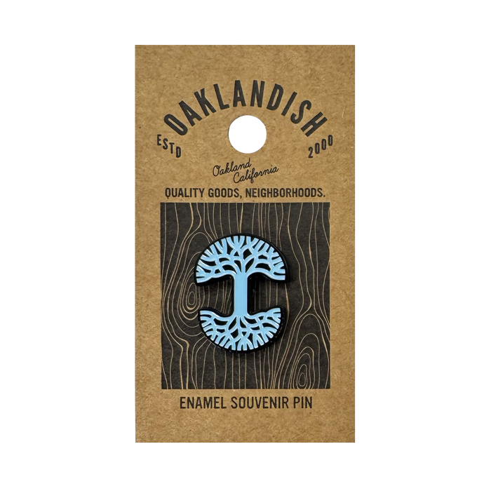 The Oaklandish Logo Enamel Pin features a blue stylized tree design and comes on a brown card reading “Oaklandish—Est’d 2000—Oakland California—Quality Goods, Neighborhoods.—Enamel Souvenir Pin.” A standout accessory.