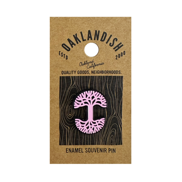The Oaklandish Logo Enamel Pin is a pink enamel accessory shaped like a stylized tree with exposed roots, attached to a brown Oaklandish card labeled “Oakland, California,” “ESTD 2000,” and “Quality Goods, Neighborhoods.”.