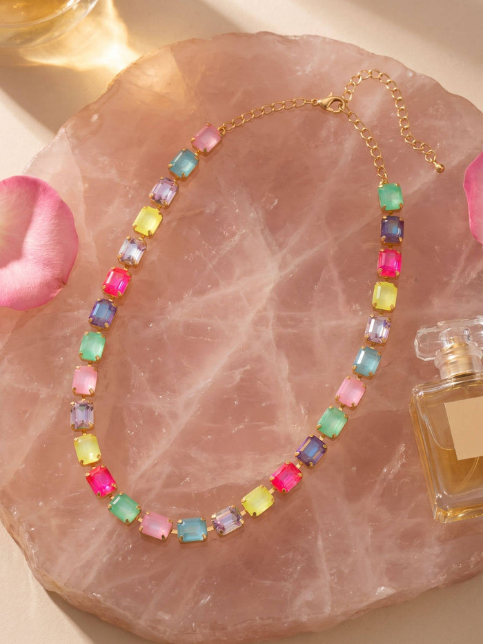 Colorful beaded necklace on a pink stone surface with a perfume bottle.