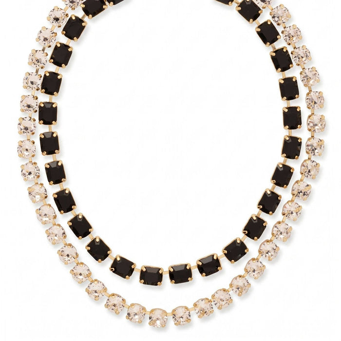 A gold-toned tennis necklace featuring two rows of stones: one row with square black gemstones and the other with round clear gemstones, set against a plain white background.