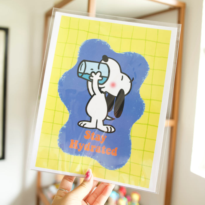 Framed print of a cartoon character holding a water bottle with 'Stay Hydrated' text, held by a hand.